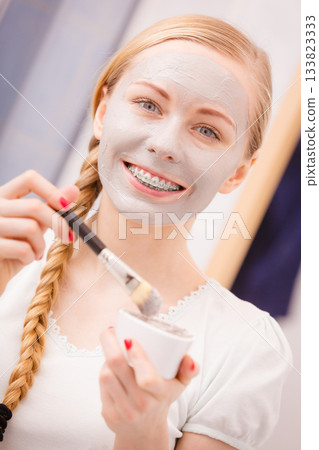Woman applying with brush clay mud mask to her face Woman applying with brush clay mud mask to her face 133823333