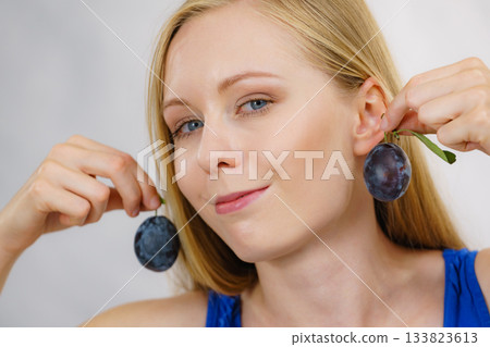 Girl holds plum fruit to her ear Girl holds plum fruit to her ear 133823613