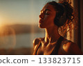 A young woman with headphones stands by the window after morning exercises. 133823715