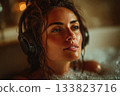 A young woman listens to music through headphones while lying in a bath with foam 133823716