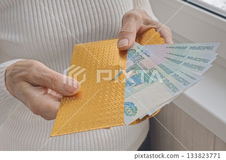 A person holding a gold envelope with a bunch of bills inside 133823771
