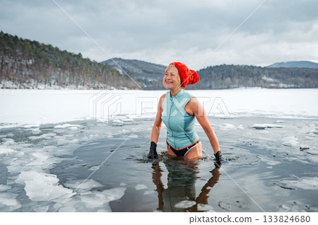 Elderly woman practicing outdoor ice bathing during winter season 133824680