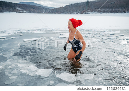 Elderly woman practicing outdoor ice bathing during winter season 133824681