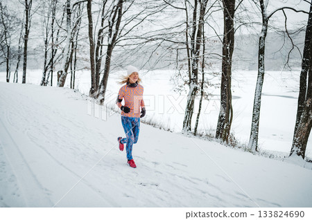 Active elderly woman jogging in cold snowy weather. Active elderly woman jogging in cold snowy weather. 133824690