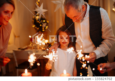 Grandparents and granddaughter holding sparklers during Christmas celebration. 133824702
