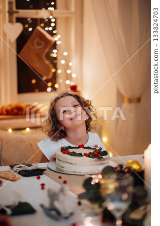 Cheerful small girl looking at christmas cake during christmas dinner. 133824703