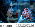 An Arab woman thoughtfully examines a 3D-printed model of her own heart, preparing for a personalized surgical procedure. Her face shows calm focus, blending tradition with cutting-edge healthcare. 133825386