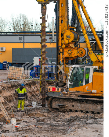 Construction worker supervising large drilling rig during foundation excavation at building site 133825438
