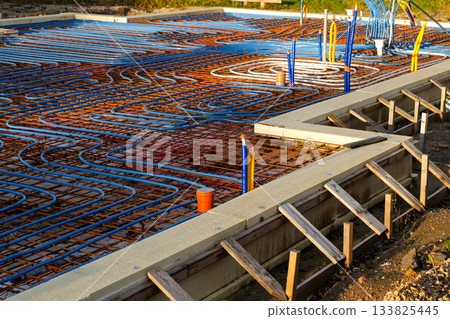 Underfloor heating pipes arranged on reinforced concrete base during modern house foundation work 133825445