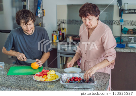 Older woman cooking lunch together with her adult son in the kitchen, enjoying a warm family moment. Home lifestyle, bonding and everyday living concept, representing connection, teamwork and positive 133825587