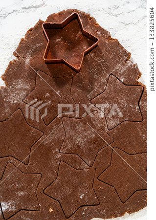 Angled close-up of chocolate dough with sharp star-shaped cutouts, ready to be transferred to a baking tray. 133825604