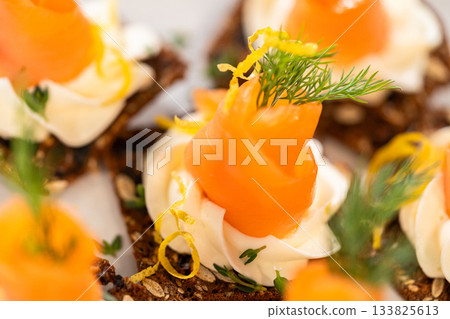 A gourmet smoked salmon canape elegantly arranged on a crispy cracker, topped with a swirl of smooth cream cheese, fresh thyme, and a drizzle of olive oil. The vibrant orange salmon contrasts A gourmet smoked salmon canape elegantly arranged on a crispy cracker, topped with a swirl of smooth cream cheese, fresh thyme, and a drizzle of olive oil. The vibrant orange salmon contrasts 133825613