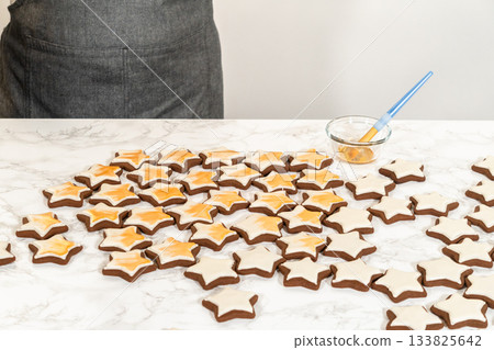 A wide spread of golden-decorated gingerbread star cookies arranged on a white surface, highlighting their intricate royal icing and elegant gold luster dust finish. A wide spread of golden-decorated gingerbread star cookies arranged on a white surface, highlighting their intricate royal icing and elegant gold luster dust finish. 133825642