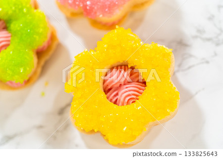 A yellow sugar-coated Easter Cookie Sandwich with Raspberry Buttercream sits on a marble background, showcasing the creamy center. A yellow sugar-coated Easter Cookie Sandwich with Raspberry Buttercream sits on a marble background, showcasing the creamy center. 133825643