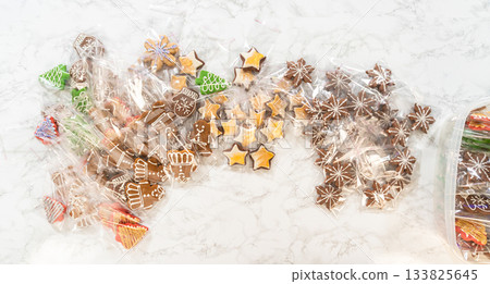 A top-down view of individually wrapped gingerbread cookies with intricate icing designs, including mittens, stars, Christmas trees, and gingerbread figures. The festive colors and details make this a 133825645