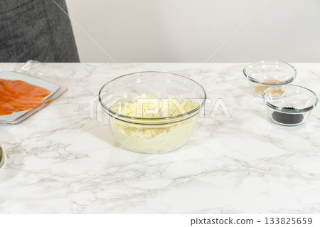 A bowl of whipped cream cheese with seasoning is set on the marble countertop, ready to be spread on smoked salmon slices for rolling. A bowl of whipped cream cheese with seasoning is set on the marble countertop, ready to be spread on smoked salmon slices for rolling. 133825659
