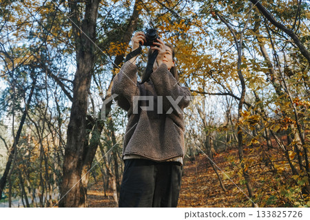 Young Woman Engaging in Photography in Sunny Autumn Forest Young Woman Engaging in Photography in Sunny Autumn Forest 133825726