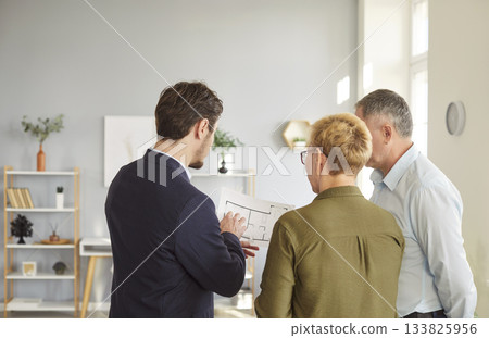 Man architect or designer showing to senior couple blueprint with design project Man architect or designer showing to senior couple blueprint with design project 133825956