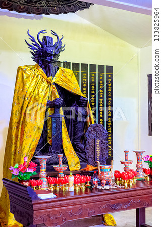 A statue of a dragon-man deity with a yellow veil and sword, surrounded by sacred texts on the walls A statue of a dragon-man deity with a yellow veil and sword, surrounded by sacred texts on the walls 133825964