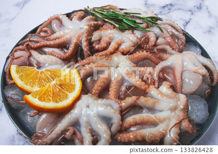 Fresh baby octopuses on ice, garnished with lemon and rosemary, on a marble table, no people, 133826428