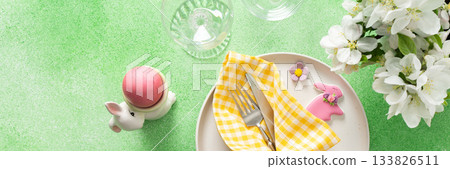 A vibrant Easter table setting features yellow checkered napkins wrapped with twine, a decorative plate, and fresh flowers, creating a festive atmosphere for spring gatherings, banner 133826511