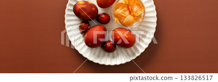 Colorful eggs are arranged on a plate alongside a small bowl of onion skins, how to dye eggs brown, creating a festive atmosphere for an Easter gathering at home, banner 133826517