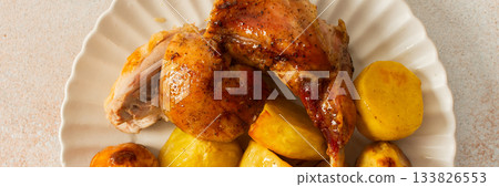A delicious plate showcases a portion of baked rabbit alongside tender, golden roasted potatoes. The rabbit appears well-seasoned, with a crispy skin, while the potatoes are perfectly cooked, banner 133826553