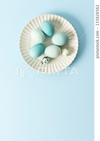 A collection of dyed blue Easter eggs arranged neatly on a white plate sits against a pastel blue background, evoking a cheerful spring atmosphere and holiday spirit 133826562