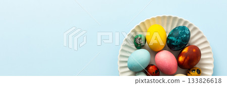 A variety of decorated Easter eggs in vibrant colors are creatively arranged on a white plate set against a soft blue background, symbolizing spring festivities and joy, banner A variety of decorated Easter eggs in vibrant colors are creatively arranged on a white plate set against a soft blue background, symbolizing spring festivities and joy, banner 133826618