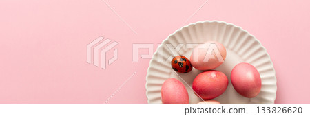 A collection of beautifully dyed Easter eggs in various shades rests on a decorative plate, set against a soft pink background, celebrating the joyful holiday spirit, banner A collection of beautifully dyed Easter eggs in various shades rests on a decorative plate, set against a soft pink background, celebrating the joyful holiday spirit, banner 133826620