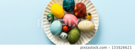 Beautifully decorated Easter eggs in vibrant colors are displayed on a white plate against a light blue background, symbolizing the joy of Easter festivities, banner 133826621