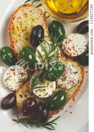 a plate with a snack, ciabatta bread with cheese and olives, olive oil, spices and herbs, top view, no people, 133827194