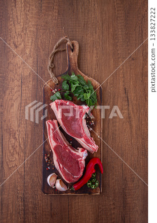 Freshly sliced lamb chops, with herbs and vegetables, on a wooden board, ready to cook, on a wooden table, 133827222