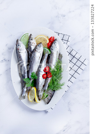 Fresh Herring fish, ready to cook, with herbs and spices, on a white platter, in the kitchen Fresh Herring fish, ready to cook, with herbs and spices, on a white platter, in the kitchen 133827224
