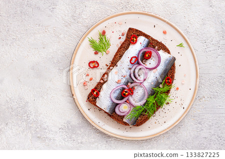 sandwiches , Herring fish, on dark rye bread, sprinkled with onion, chili pepper and herbs, on a light plate 133827225