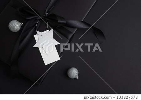 Black Christmas Gift Box with Satin Ribbon and White Blanck Label on Dark Holiday Background Black Christmas Gift Box with Satin Ribbon and White Blanck Label on Dark Holiday Background 133827578