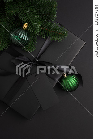 Black Christmas Gift Box with Satin Ribbon and Green Ornaments on Dark Holiday Background 133827584