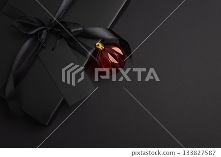 Black Christmas Gift Box with Satin Ribbon and Red Ornaments on Dark Holiday Background 133827587