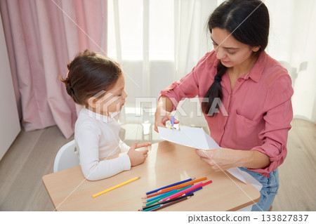 Mother and daughter cutting designs from paper with scissors for an art project 133827837