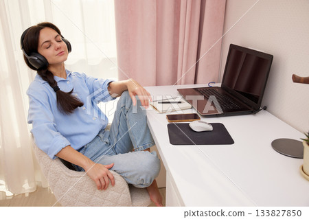 Woman with headphones relaxing at home desk, taking a calm music break from work Woman with headphones relaxing at home desk, taking a calm music break from work 133827850