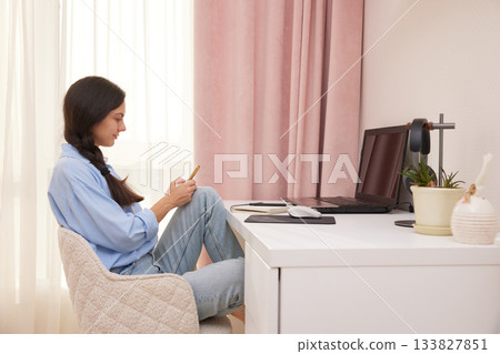 Woman playing with smartphone at desk, avoiding work on laptop in home office 133827851