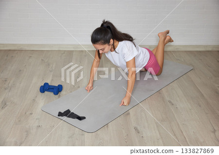 Woman exercising on yoga mat with dumbbells nearby, practicing push-ups for fitness 133827869
