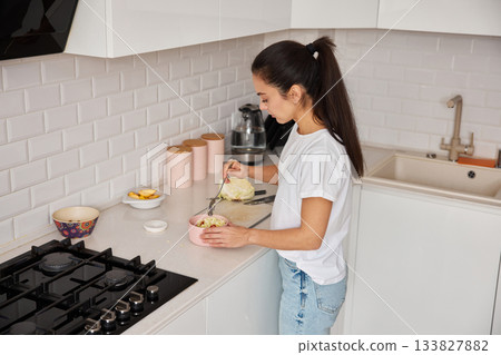 Woman standing in modern kitchen, mixing a fresh salad in a bowl for a healthy meal 133827882
