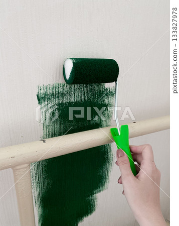 Person engaged in home improvement project, painting wall with dark green color using small roller. Woman hand grips roller, which smoothly rolling paint onto surface. Interior design and improvement Person engaged in home improvement project, painting wall with dark green color using small roller. Woman hand grips roller, which smoothly rolling paint onto surface. Interior design and improvement 133827978