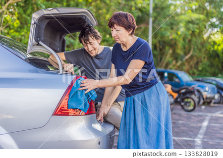 Older woman washing a car together with her adult son, enjoying a productive family moment outdoors. Teamwork, care, bonding and lifestyle concept, showing cooperation, connection and everyday chores Older woman washing a car together with her adult son, enjoying a productive family moment outdoors. Teamwork, care, bonding and lifestyle concept, showing cooperation, connection and everyday chores 133828019