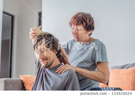 Older woman giving her adult son a shoulder and arm stretch massage at home, creating a warm family moment focused on care, relaxation and wellbeing. Wellness, support, bonding and healthy lifestyle Older woman giving her adult son a shoulder and arm stretch massage at home, creating a warm family moment focused on care, relaxation and wellbeing. Wellness, support, bonding and healthy lifestyle 133828024