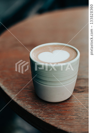 A beautiful cappuccino cup with latte art in a heart shape sits on a rustic wooden table. The warm tones create a cozy feel. A heart-shaped milky foam A beautiful cappuccino cup with latte art in a heart shape sits on a rustic wooden table. The warm tones create a cozy feel. A heart-shaped milky foam 133828360