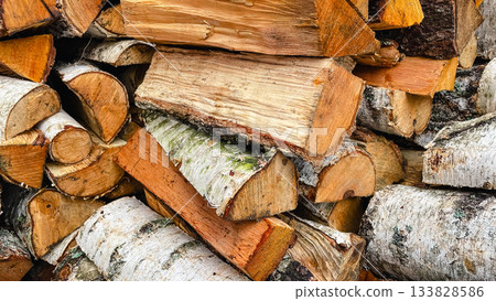 Detailed close-up of stacked birch firewood logs, showing white bark and rough textured wood ends Detailed close-up of stacked birch firewood logs, showing white bark and rough textured wood ends 133828586
