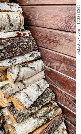 Neatly stacked birch firewood logs against a textured brown wooden wall. Rustic natural background for design Neatly stacked birch firewood logs against a textured brown wooden wall. Rustic natural background for design 133828593