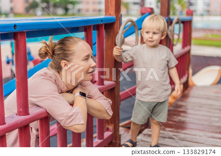 A mother playing with her young son at an outdoor playground, enjoying joyful family time and positive parenting moments. Childhood fun, bonding, laughter and carefree early years concept A mother playing with her young son at an outdoor playground, enjoying joyful family time and positive parenting moments. Childhood fun, bonding, laughter and carefree early years concept 133829174